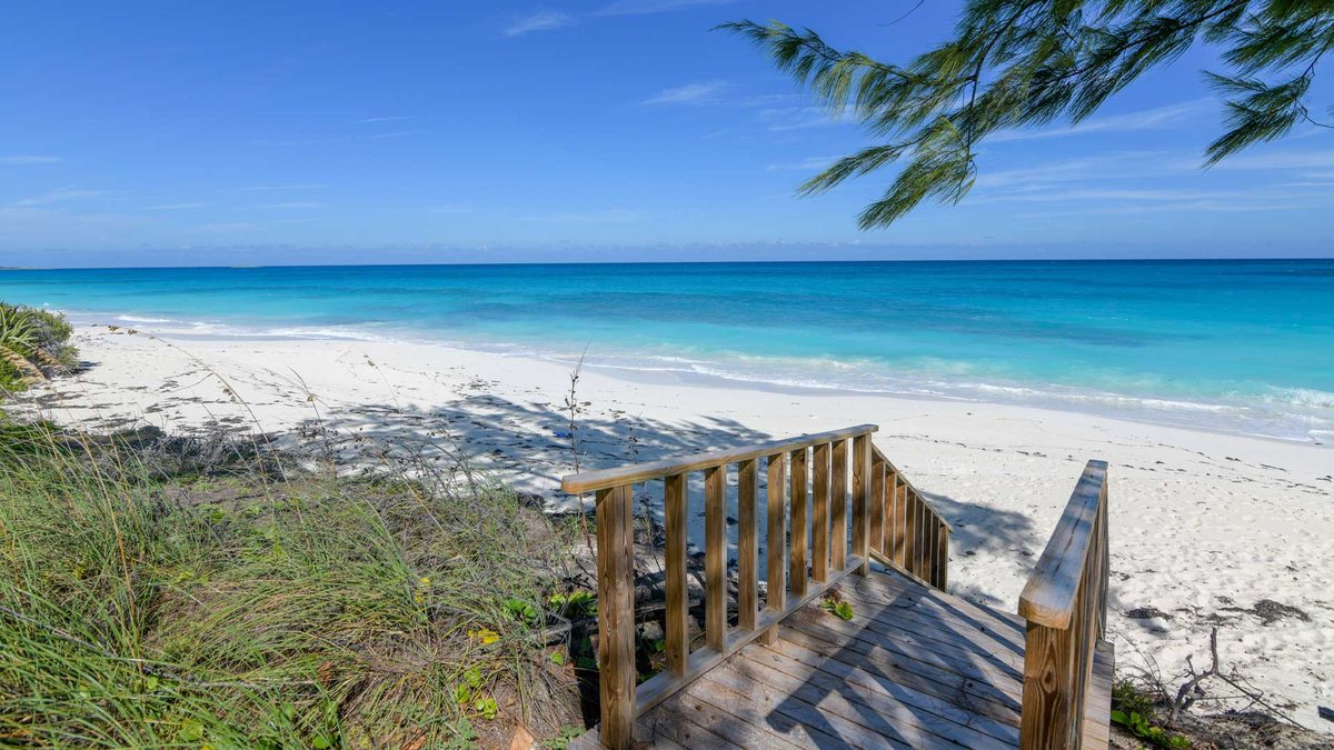 A wooden boardwalk leading down to a quiet white-sand beach on Great Exuma